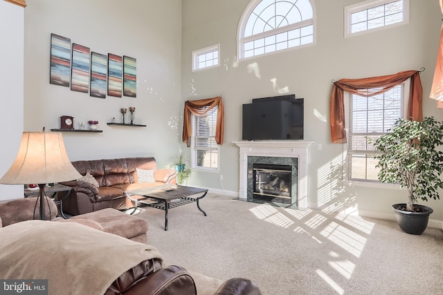 carpeted living area featuring a high ceiling, a fireplace, baseboards, and a wealth of natural light