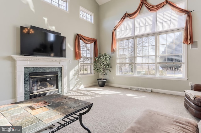 carpeted living area featuring a towering ceiling, baseboards, a premium fireplace, and visible vents