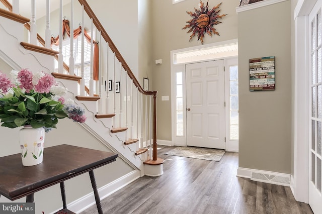 foyer entrance with a high ceiling, visible vents, baseboards, and wood finished floors