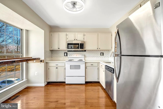 kitchen with light countertops, appliances with stainless steel finishes, light wood-style flooring, and decorative backsplash