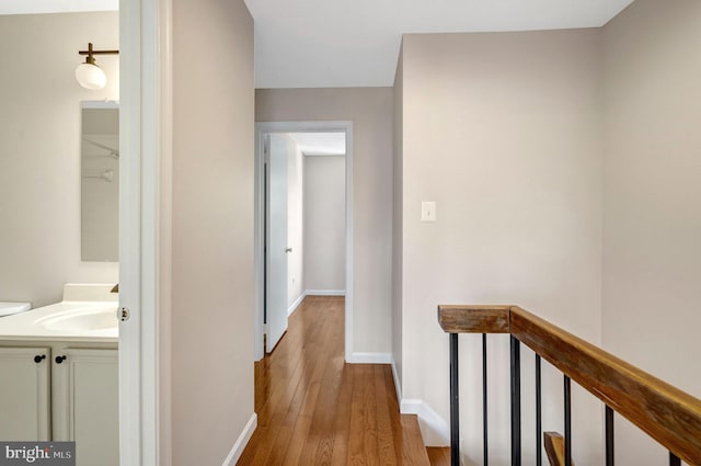 hallway featuring a sink, baseboards, hardwood / wood-style floors, and an upstairs landing