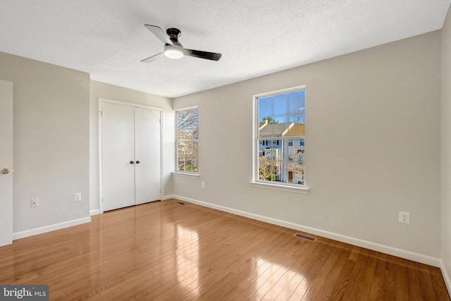 unfurnished bedroom featuring wood-type flooring, visible vents, a textured ceiling, and multiple windows