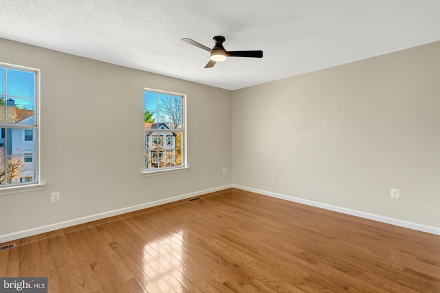 spare room with wood-type flooring, visible vents, a ceiling fan, a textured ceiling, and baseboards