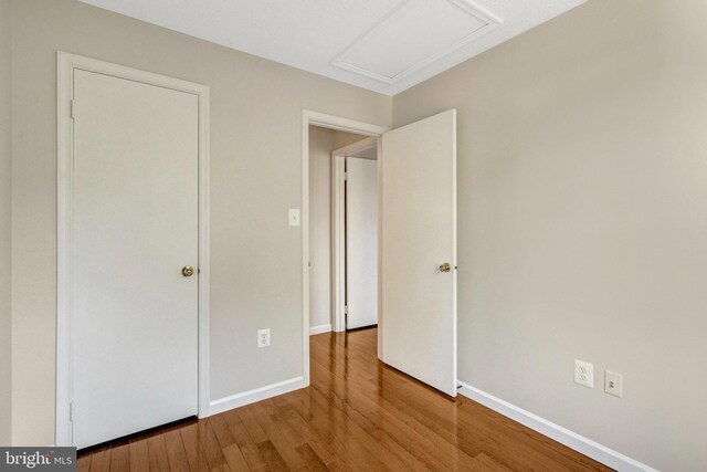 unfurnished bedroom with attic access, baseboards, and wood finished floors