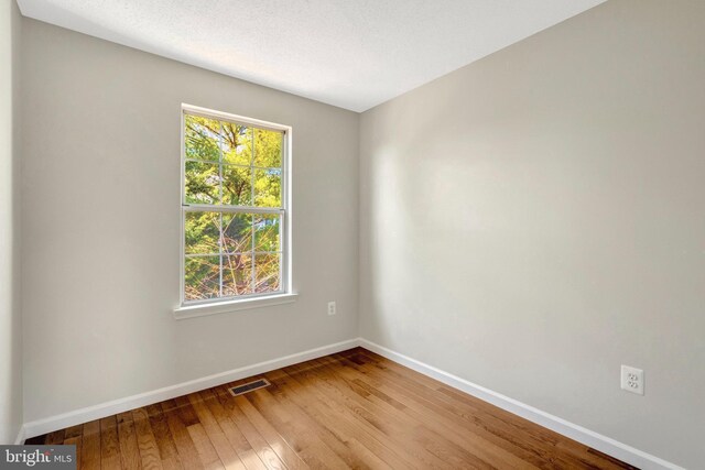 spare room featuring hardwood / wood-style flooring, baseboards, visible vents, and a textured ceiling