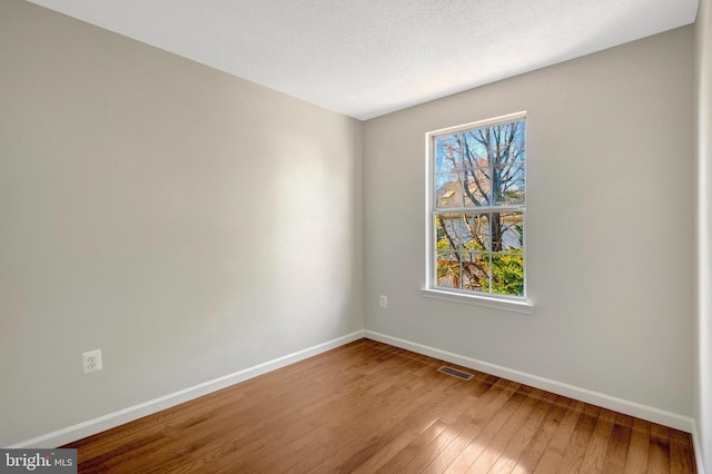 empty room with wood-type flooring, visible vents, a textured ceiling, and baseboards