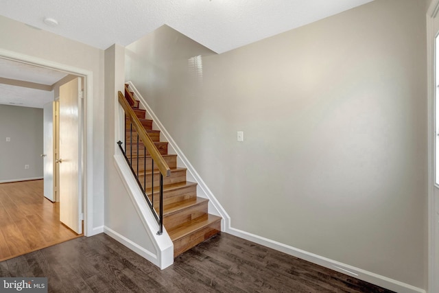 staircase with a textured ceiling, baseboards, and wood finished floors