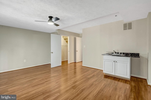 unfurnished living room with light wood-style flooring, visible vents, ceiling fan, and a sink