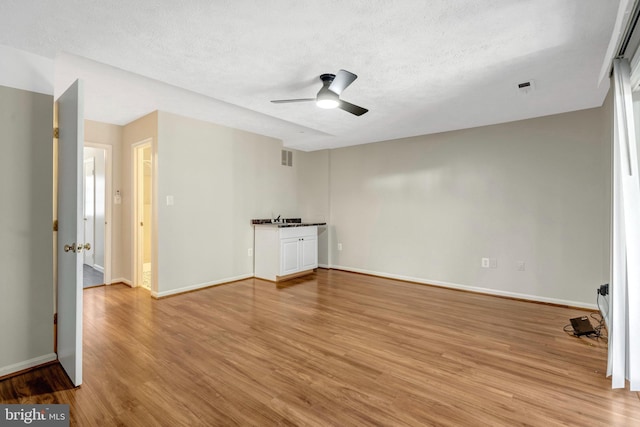 empty room with light wood finished floors, baseboards, and a textured ceiling