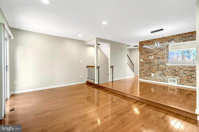 interior space with visible vents, baseboards, hardwood / wood-style flooring, brick wall, and stairway