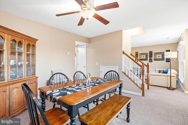 dining room with stairway, light colored carpet, baseboards, and ceiling fan