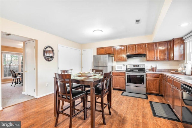 kitchen featuring visible vents, under cabinet range hood, light wood-style floors, brown cabinetry, and stainless steel appliances