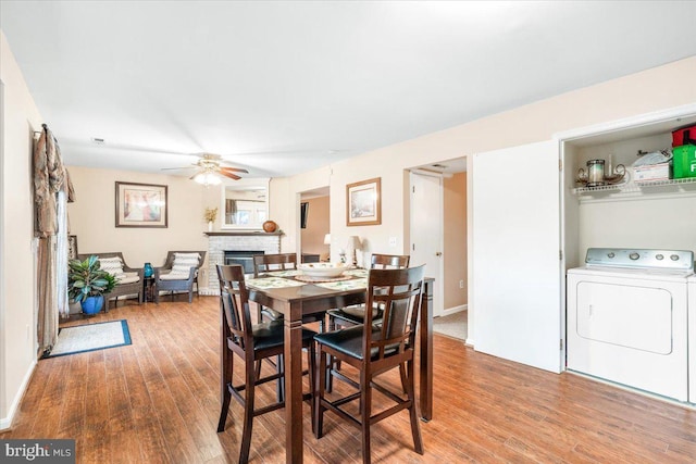 dining space featuring washer / dryer, wood finished floors, a fireplace, and ceiling fan