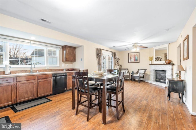 dining area with a ceiling fan, a brick fireplace, light wood-style flooring, and visible vents