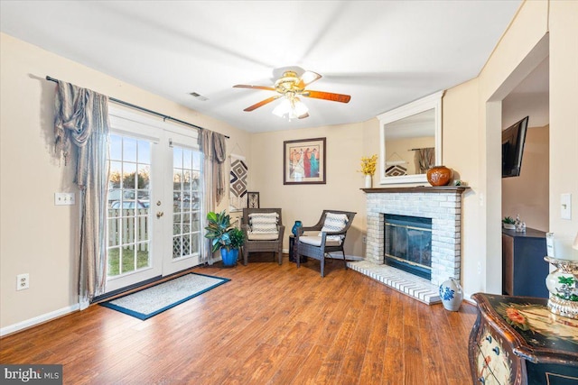 living area featuring visible vents, a ceiling fan, wood finished floors, baseboards, and a brick fireplace