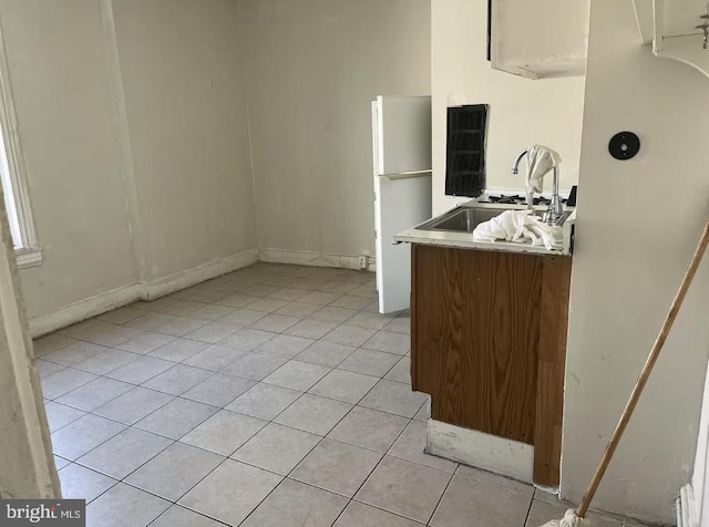 kitchen featuring freestanding refrigerator, light tile patterned flooring, and a sink