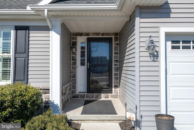 doorway to property with stone siding, roof with shingles, and an attached garage