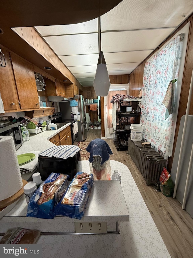 kitchen featuring brown cabinets, stainless steel appliances, light countertops, wood walls, and light wood-style floors