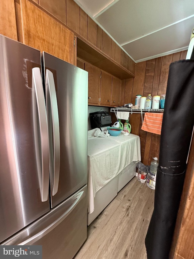 kitchen with brown cabinetry, light wood-type flooring, freestanding refrigerator, and wooden walls