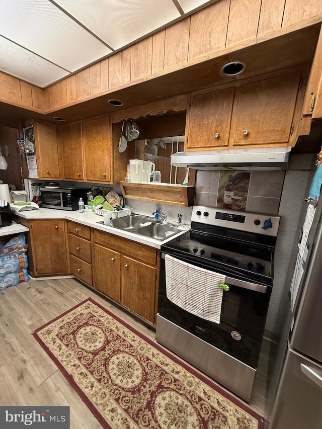 kitchen with light wood finished floors, appliances with stainless steel finishes, brown cabinets, light countertops, and a sink