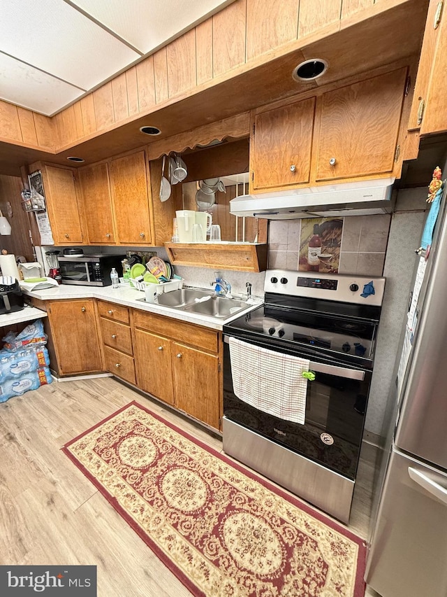 kitchen with light wood finished floors, stainless steel appliances, light countertops, a sink, and under cabinet range hood