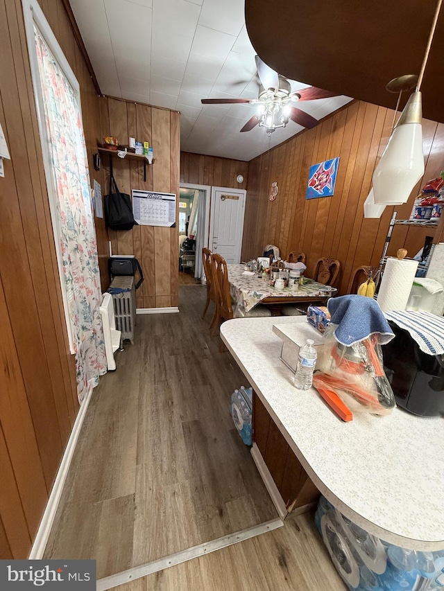 dining room with baseboards, wood finished floors, a ceiling fan, and wooden walls