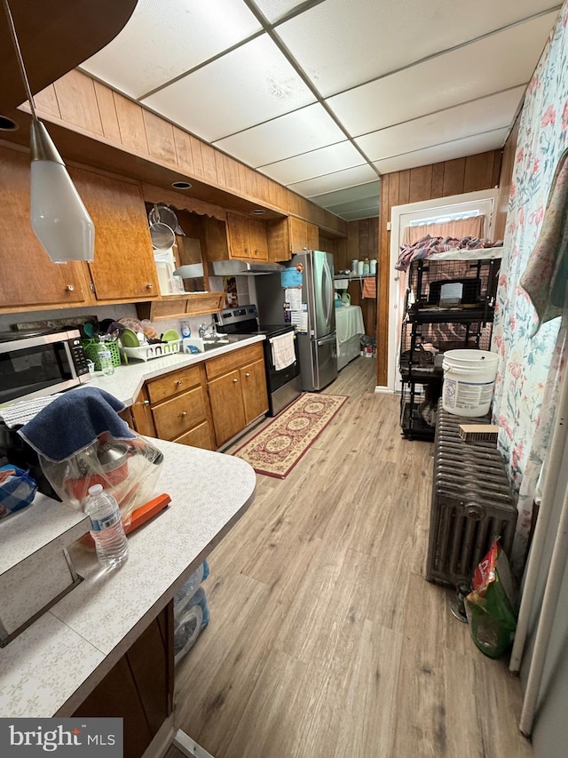 kitchen featuring stainless steel appliances, light countertops, brown cabinetry, light wood-style floors, and wooden walls