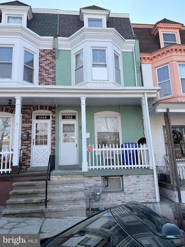 townhome / multi-family property featuring a porch, roof with shingles, brick siding, and mansard roof