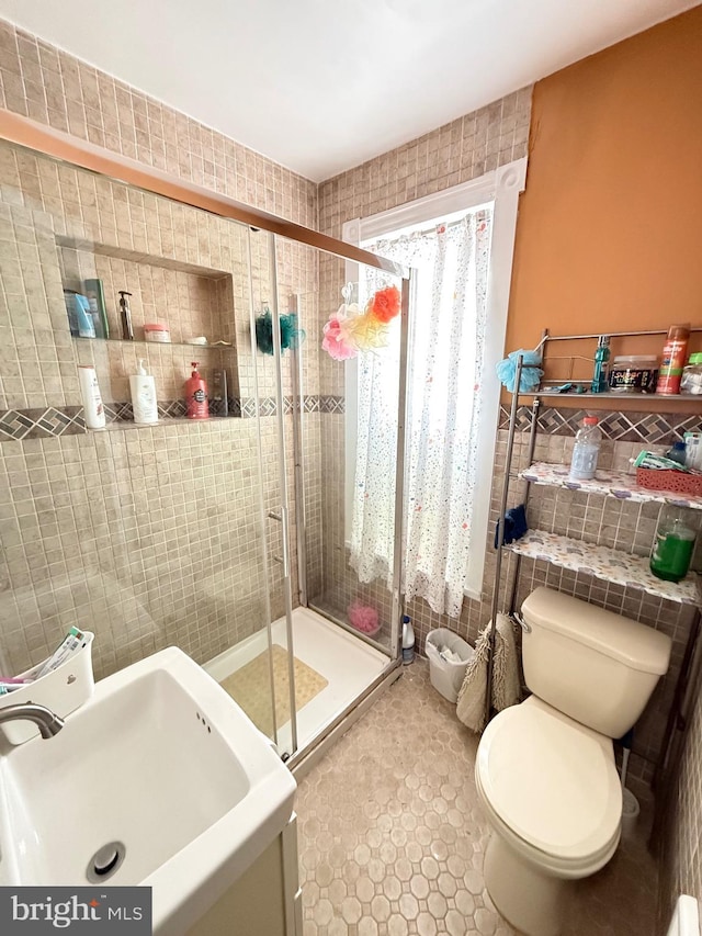 full bath with a sink, a stall shower, toilet, and tile walls