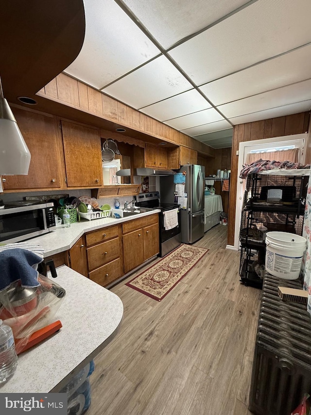 kitchen featuring light wood-style flooring, stainless steel appliances, light countertops, open shelves, and brown cabinetry