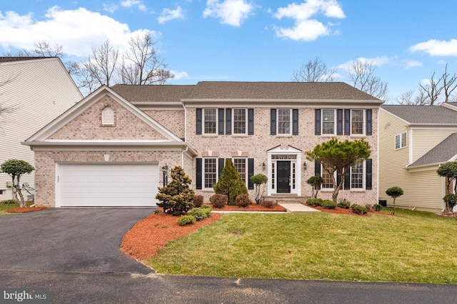 colonial inspired home with an attached garage, a front lawn, aphalt driveway, and brick siding