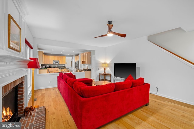 living area with light wood-style floors, a fireplace, baseboards, and a ceiling fan