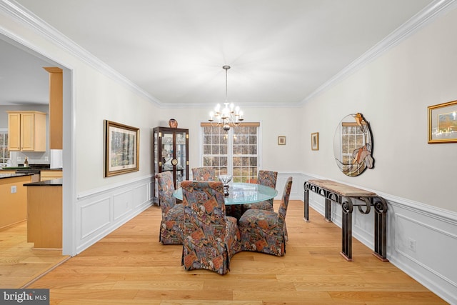 dining space featuring a chandelier, a wainscoted wall, light wood-style floors, and ornamental molding