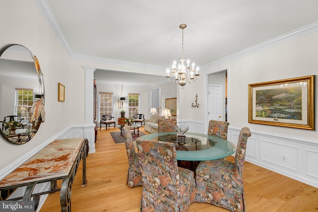 dining room with a notable chandelier, light wood-type flooring, decorative columns, and crown molding