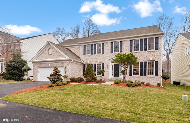 colonial inspired home with a garage, a front yard, aphalt driveway, and brick siding