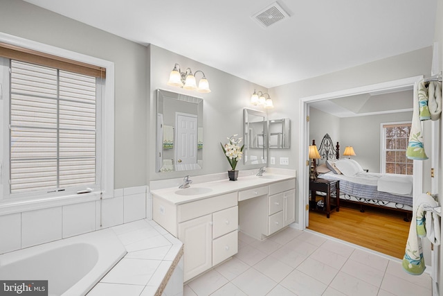 ensuite bathroom with a relaxing tiled tub, visible vents, ensuite bath, tile patterned floors, and a sink