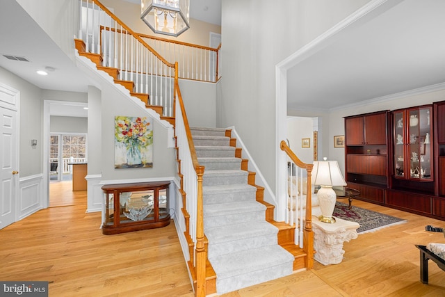 stairway with a towering ceiling, crown molding, visible vents, and wood finished floors