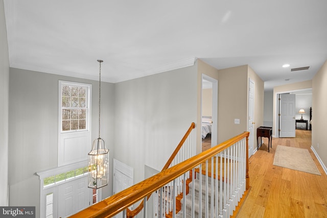 corridor featuring an upstairs landing, baseboards, ornamental molding, light wood finished floors, and an inviting chandelier