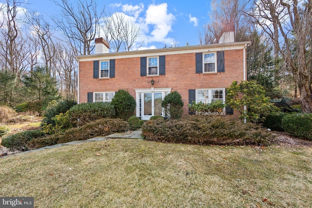 colonial home featuring a chimney, a front lawn, and brick siding