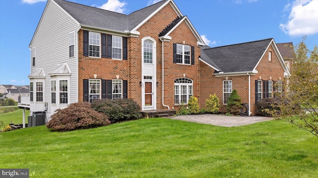 view of front of home featuring brick siding, roof with shingles, a front lawn, and central air condition unit