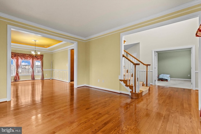 spare room featuring an inviting chandelier, crown molding, stairway, and wood finished floors