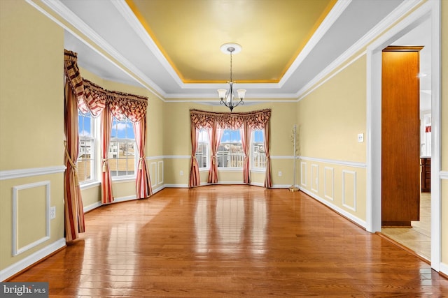 spare room featuring crown molding, a raised ceiling, a chandelier, baseboards, and hardwood / wood-style flooring