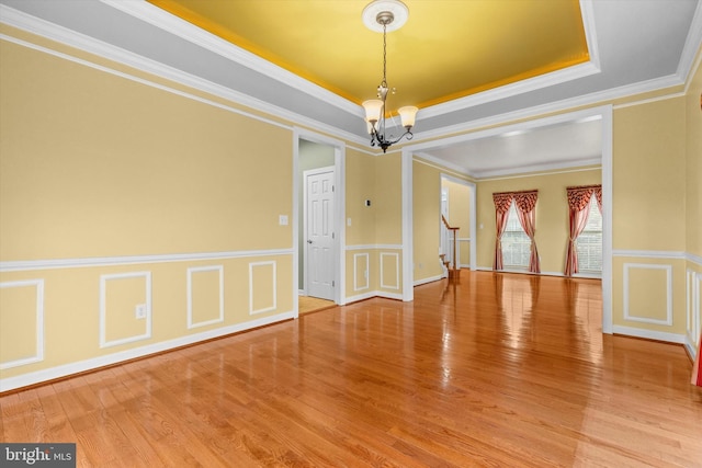 empty room featuring stairway, wood finished floors, a tray ceiling, crown molding, and a notable chandelier