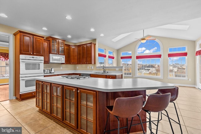 kitchen with white appliances, a sink, light countertops, a center island, and glass insert cabinets