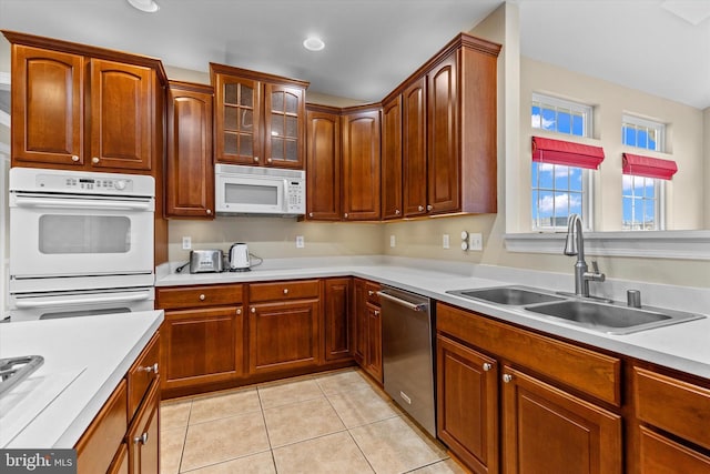 kitchen featuring light tile patterned floors, white appliances, a sink, light countertops, and glass insert cabinets