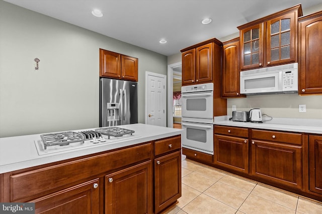 kitchen with light tile patterned floors, recessed lighting, white appliances, light countertops, and glass insert cabinets