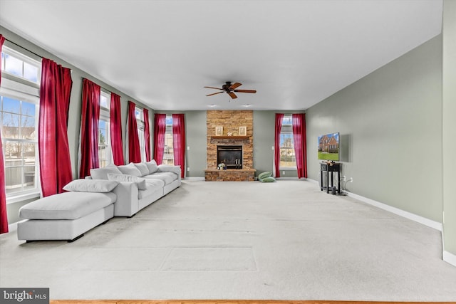 living room with carpet, baseboards, a ceiling fan, and a stone fireplace