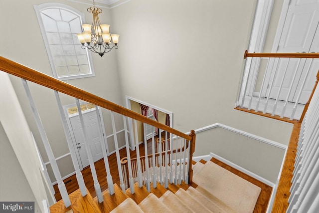 stairs featuring baseboards, a towering ceiling, an inviting chandelier, and wood finished floors