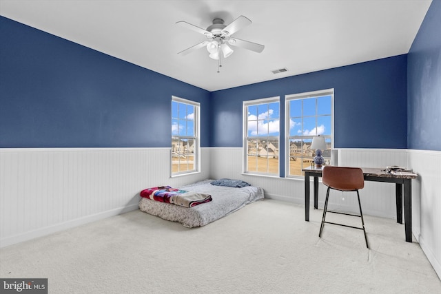 bedroom with a wainscoted wall, carpet, visible vents, and a ceiling fan