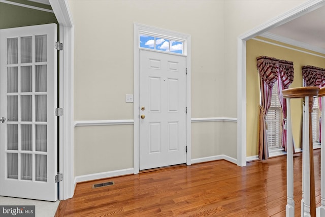 foyer featuring visible vents, crown molding, baseboards, and wood finished floors